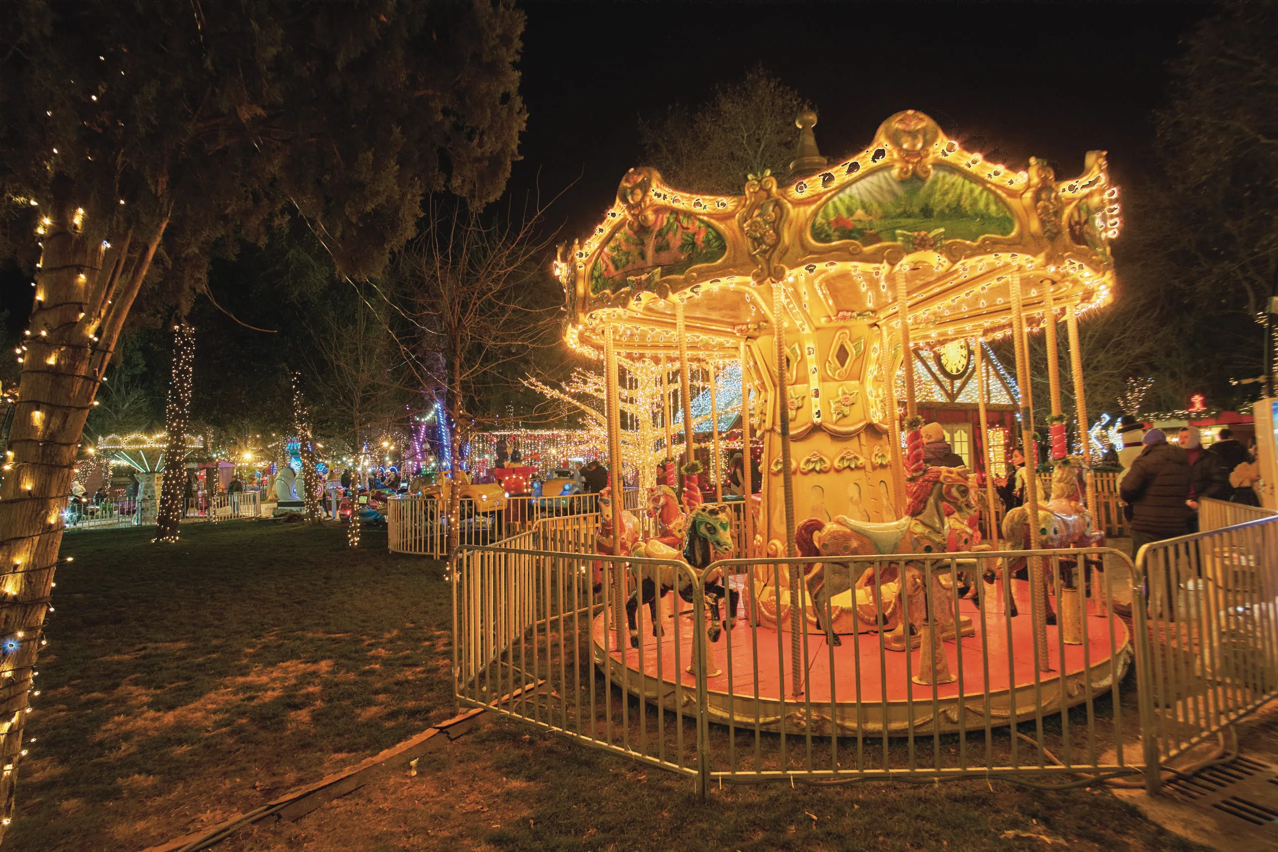 A lit carousel turning in a park at night, strung with lights
