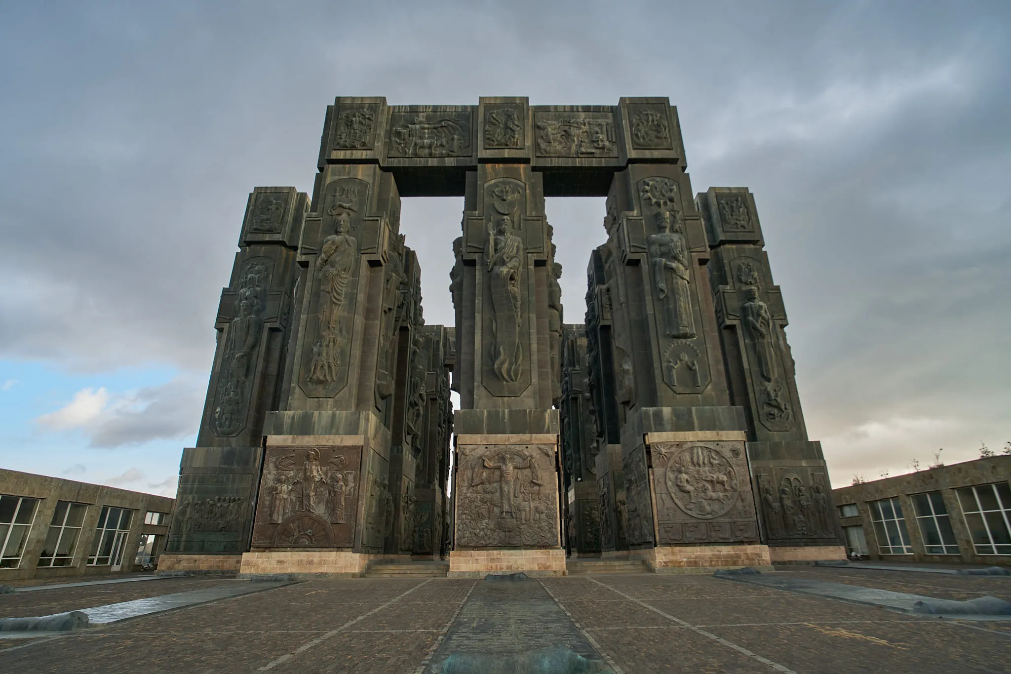 Monumental carved stone pillars standing against a clouded sky