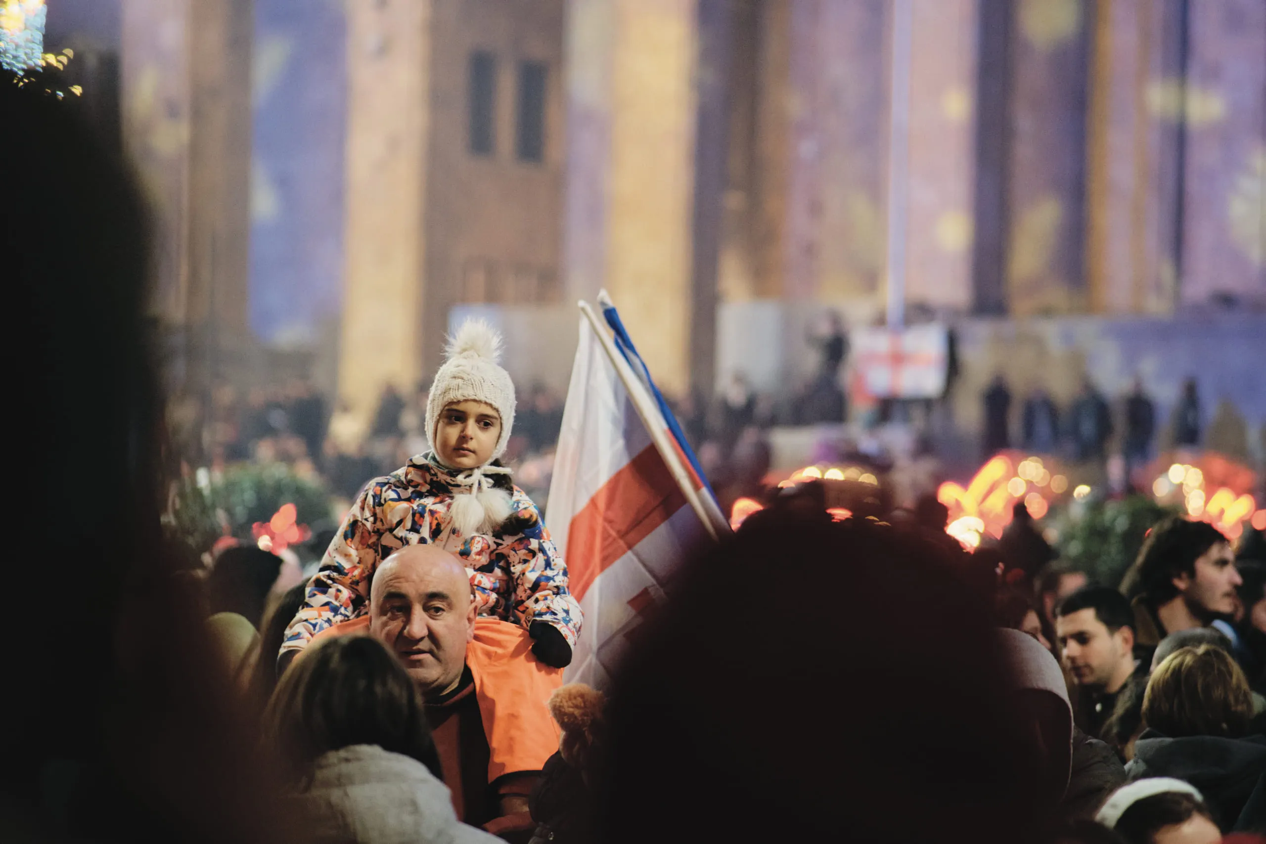 A dense night crowd with a flag raised, floodlit columns behind