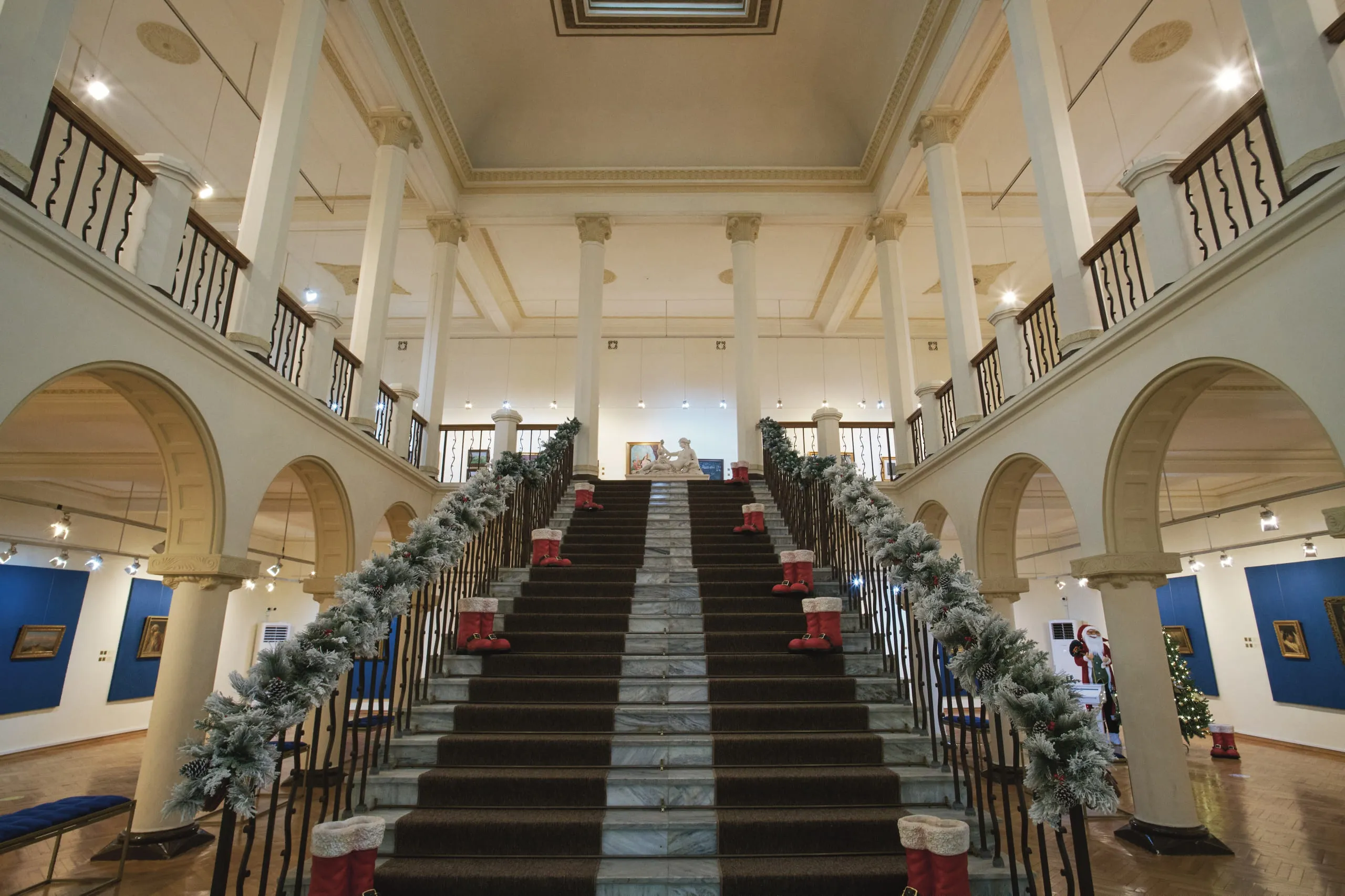 A grand museum staircase hung with garlands, under an arcaded gallery