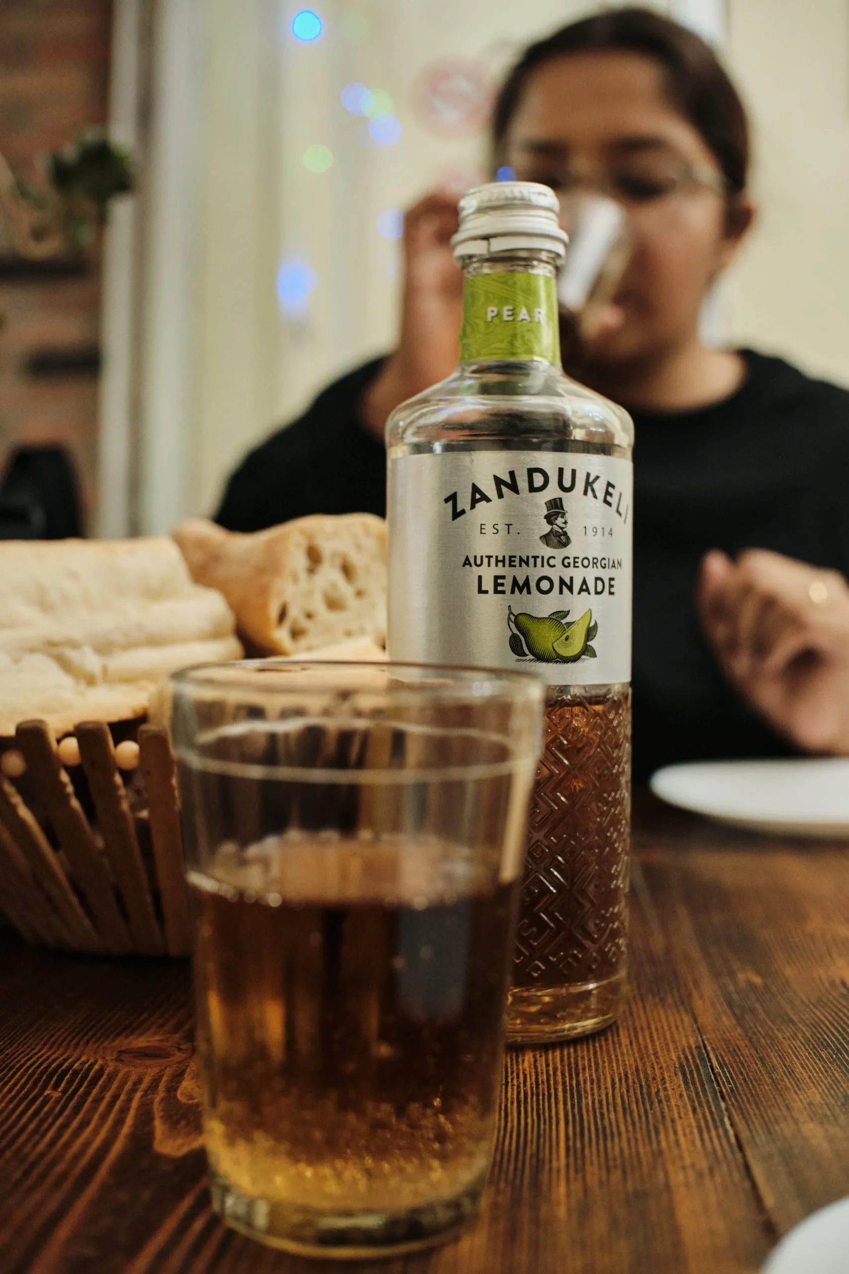 A bottle of Georgian pear lemonade and a filled glass on a wooden table
