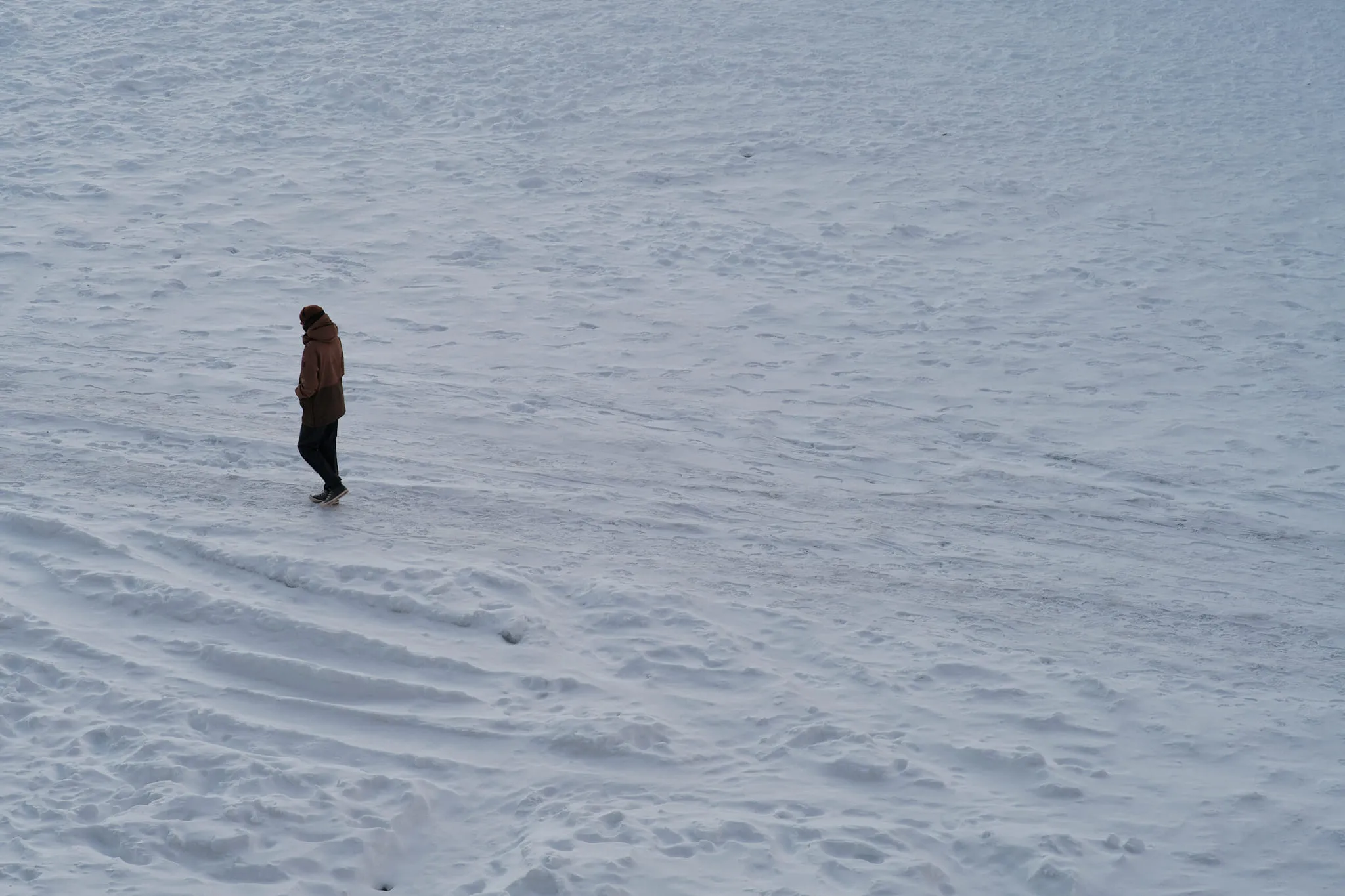 A single small figure crossing a wide empty snowfield