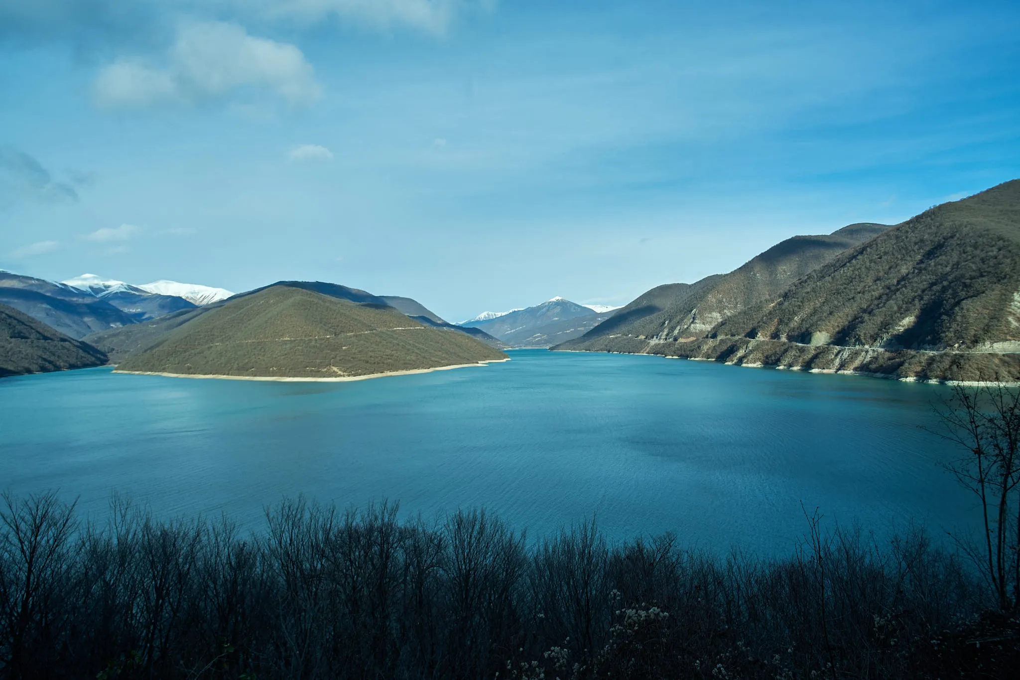 A turquoise reservoir held between bare winter hills
