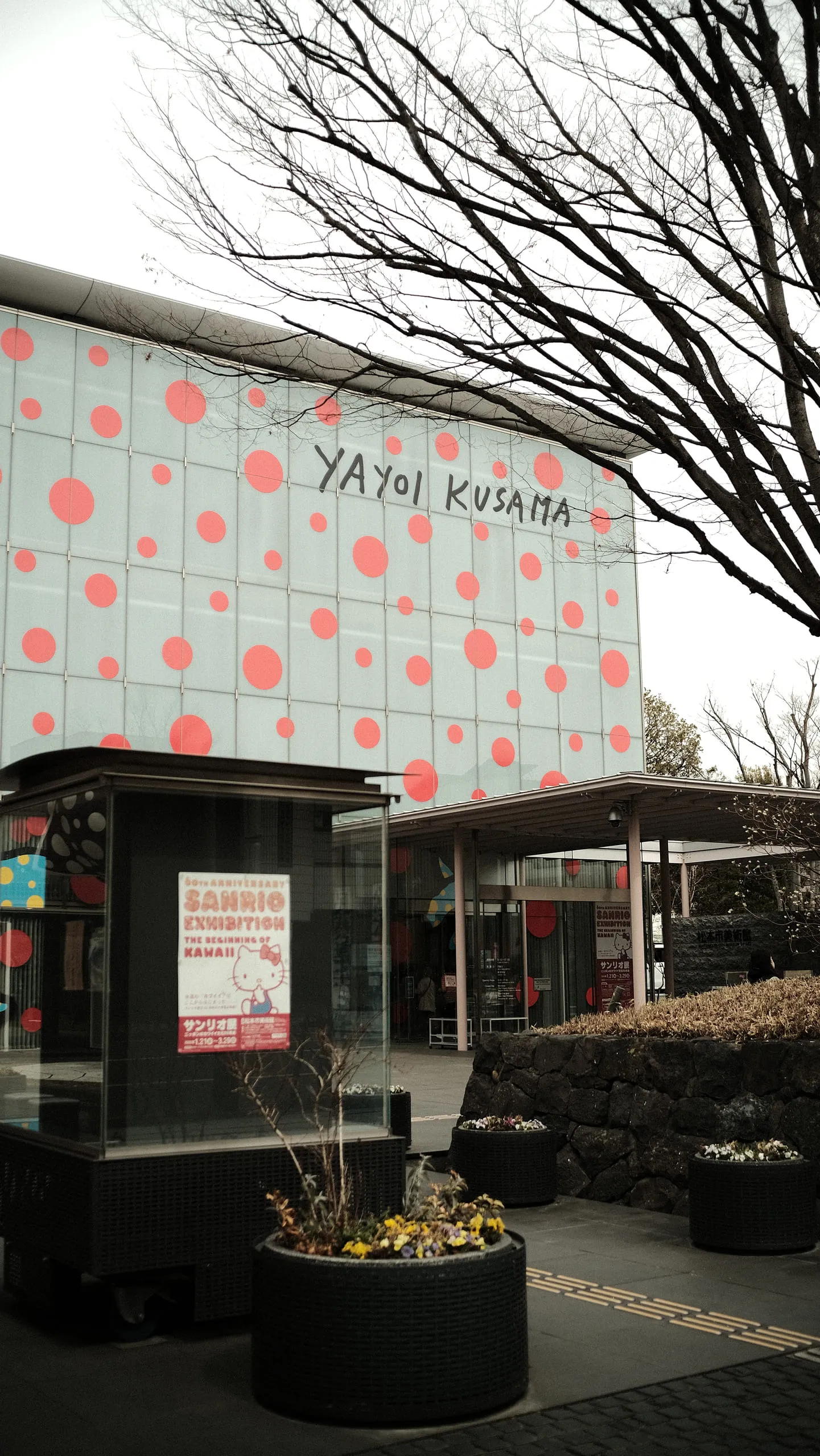 The corner of a museum building covered in large red polka dots, with YAYOI KUSAMA lettered across it